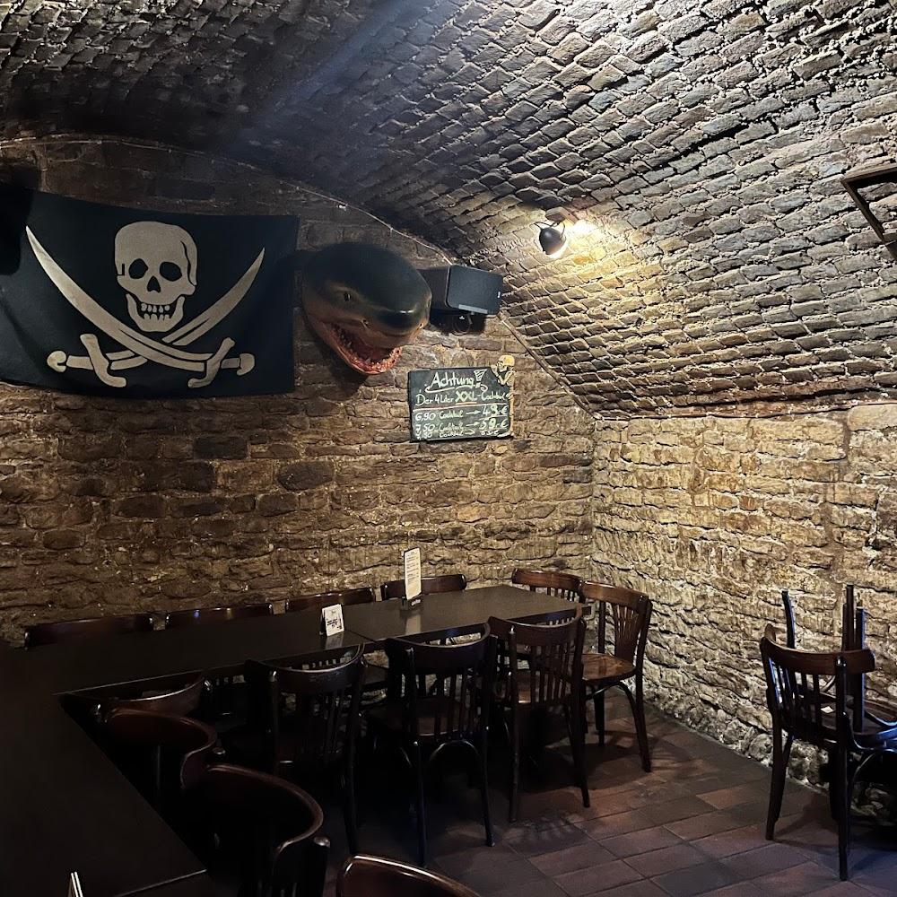 A stone cellar with a pirate flag, a shark head, and a table with chairs.